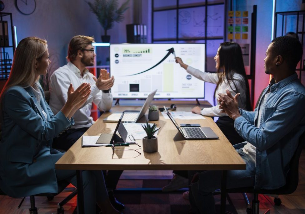 Asian woman presenting financial report of worldwide economy on big monitor during meeting with international partners. Focus on the table with gadgets