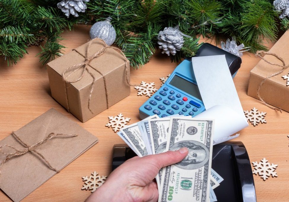 Christmas sale. The hand holds cash to pay for gifts for the holidays. Buying New Year's gifts. Cash register, receipt, gifts, Christmas decoration on the table
