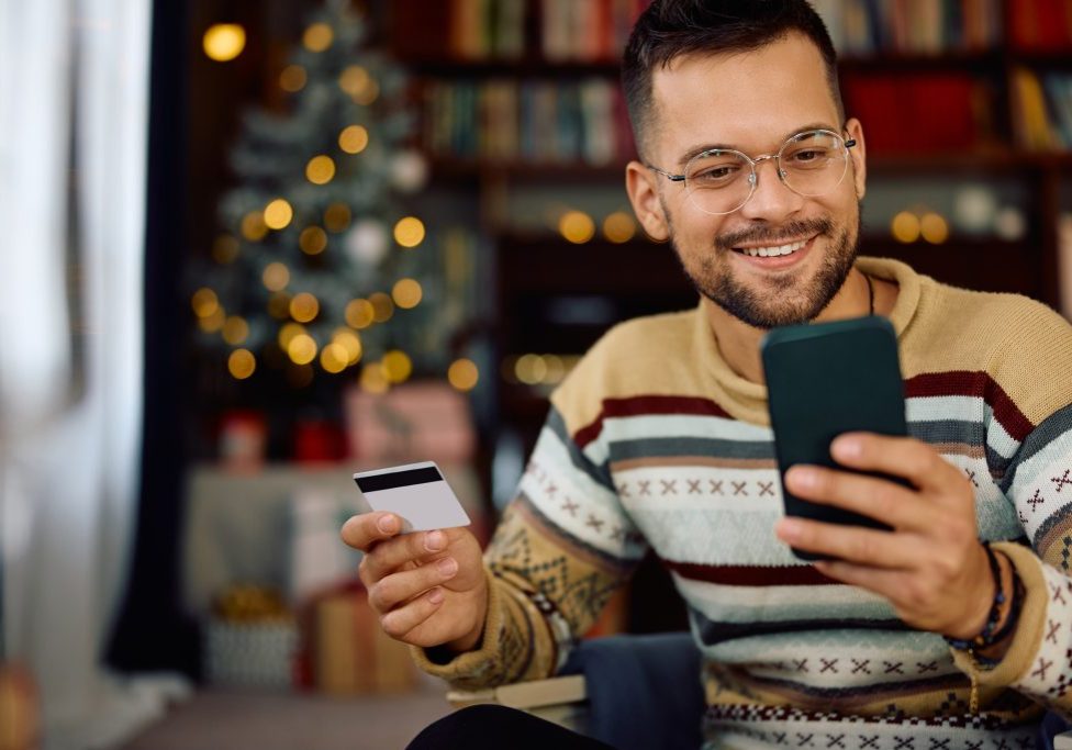 Happy man buying online with credit card and smart phone during Christmas holidays.