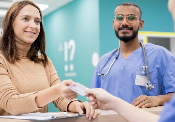Young cheerful patient giving credit card to receptionist in clinics to pay for medical service after consultation and treatment