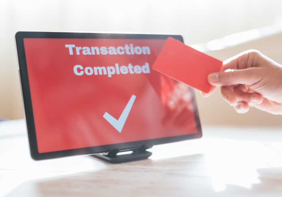 Person holding red credit card over tablet showing a checkmark and transaction completed, symbolizing secure, fast online payment for shopping and digital banking convenience